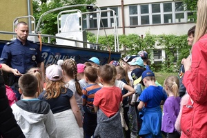 Policjant na tle łodzi, wokół niego stoją dzieci