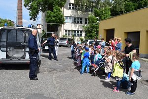 Dwóch policjantów stoi przy radiowozie, wokół przedszkolaki