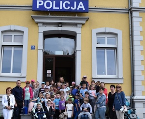 Przedszkolaki, ich wychowawcy, policjant i pracownik Policji soją na schodach przed Komendą