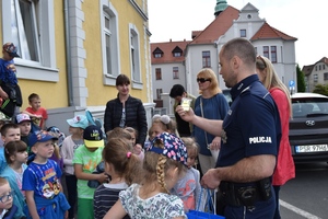 Policjant trzyma w ręce element odblaskowy i prezentuje go stojącym przy nim dzieciom