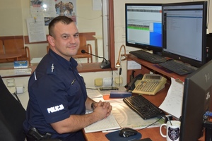 Policjant na Stanowisku Kierowania. Siedzi przed komputerami i telefonami w swoim miejscu pełnienia służby.