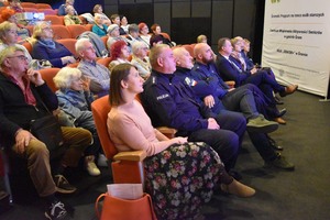 Uczestnicy spotkania, seniorzy i organizatorzy, siedzą na widowni kinoteatru.
