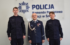 Dwaj nowi policjanci stoją wspólnie z Komendantem w sali konferencyjnej śremskiej Policji.