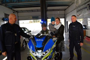 Dziecko siedzi na policyjnym motocyklu, obok stoi kobieta z dzieckiem i policjanci.