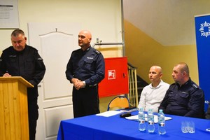 Policjant stoi i zwraca się do uczestników debaty.