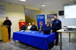 Policjant stoi i zwraca się do uczestników debaty.