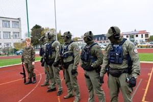 Policjanci i uczeń stoją na boisku szkolnym.