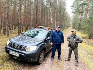 Policjant i strażnik leśny stoją w lesie przy samochodzie.