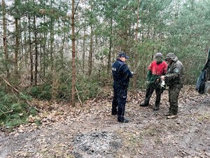 Policjant i strażnik leśny stoją w lesie i legitymują osobę.