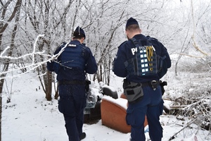 Dwóch policjantów stoi wśród drzew i śniegu, przy pokojowych fotelach.