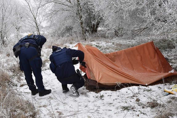 Dwóch policjantów zagląda do namiotu.